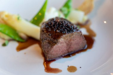 Kızarmış sığır filetosu, beyaz kuşkonmaz ve bezelye ile servis ediliyor.