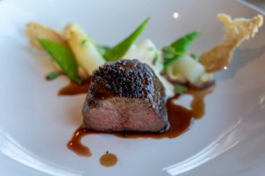 Kızarmış sığır filetosu, beyaz kuşkonmaz ve bezelye ile servis ediliyor.