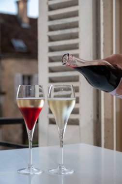 Kir Royal içen, Fransız aperatifi. Krema ve şampanyayla kaplanmış, genellikle flüt bardaklarıyla servis edilen, eski Fransız köyü manzaralı.