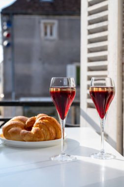 Kir Royal içen, Fransız aperatifi. Krema ve şampanyayla kaplanmış, genellikle flüt bardaklarıyla servis edilen, eski Fransız köyü manzaralı.