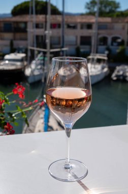 Fransız Riviera Cote d 'Azur' da yaz mevsimi, Cotes de Provence 'den soğuk gül şarabı içmek Port Grimaud, Var, Fransa' da güneşli açık teraslarda arka planda botlar ve yatlarla