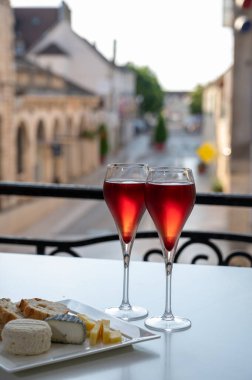 Kir Royal içen, Fransız aperatifi. Krema ve şampanyayla kaplanmış, genellikle flüt bardaklarıyla servis edilen, eski Fransız köyü manzaralı.