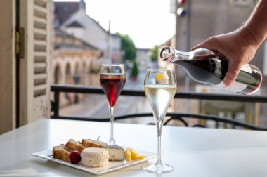 Kir Royal içen, Fransız aperatifi. Krema ve şampanyayla kaplanmış, genellikle flüt bardaklarıyla servis edilen, eski Fransız köyü manzaralı.