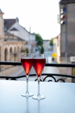 Kir Royal içen, Fransız aperatifi. Krema ve şampanyayla kaplanmış, genellikle flüt bardaklarıyla servis edilen, eski Fransız köyü manzaralı.