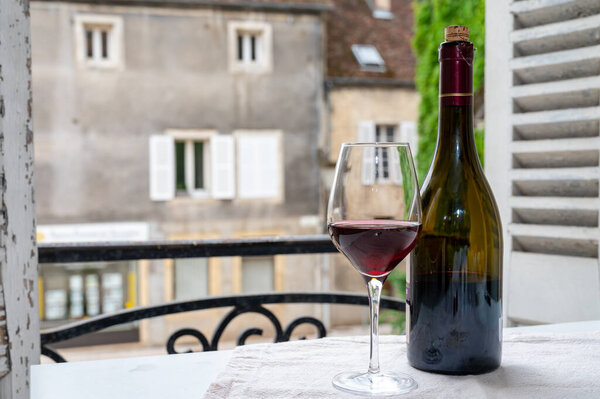 Дегустация бордового красного вина с виноградников Grand Cru pinot noir, бокал и бутылка красного вина и вид на старую улицу города в винном регионе Бургундии, Франция