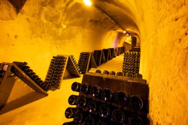 Derin ve uzun yeraltı mağaralarındaki raflarda şişeler şarap ve üzüm şarabından şampanya yapıyor Reims, Champagne, France 'ta.