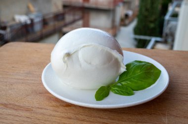 İtalyan yumuşak peynirli beyaz top Mozzarella di Bufala Campana ve taze yeşil fesleğen arka planda İtalyan evleriyle servis edilir.