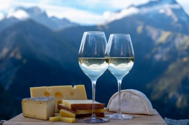 Fransa 'nın Savoy bölgesinden lezzetli peynir ve şarap, Beaufort, abondance, emmental, tomme ve reblochon de savoie peynirleri ve yazın açık havada sunulan beyaz şarap arka planda Alp dağlarının zirveleri