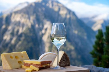Fransa 'nın Savoy bölgesinden lezzetli peynir ve şarap, Beaufort, abondance, emmental, tomme ve reblochon de savoie peynirleri ve yazın açık havada sunulan beyaz şarap arka planda Alp dağlarının zirveleri