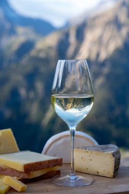 Fransa 'nın Savoy bölgesinden lezzetli peynir ve şarap, Beaufort, abondance, emmental, tomme ve reblochon de savoie peynirleri ve yazın açık havada sunulan beyaz şarap arka planda Alp dağlarının zirveleri