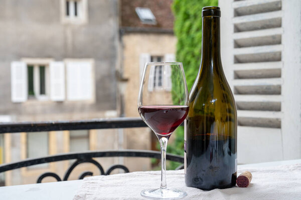Дегустация бордового красного вина с виноградников Grand Cru pinot noir, бокал и бутылка красного вина и вид на старую улицу города в винном регионе Бургундии, Франция