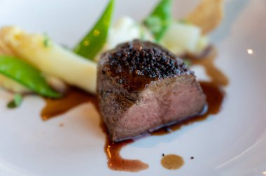 Kızarmış sığır filetosu, beyaz kuşkonmaz ve bezelye ile servis ediliyor.