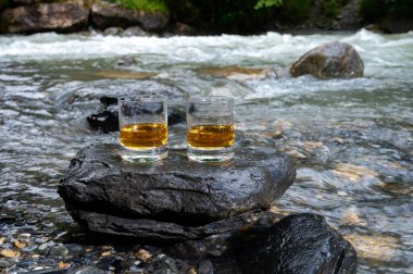 Bir bardak sert viski, arka planda hızlı akan dağ nehri olan viski, İskoçya.