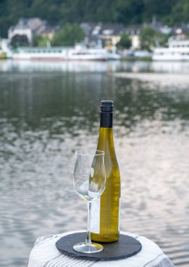 Mosel şarap bölgesinde beyaz kaliteli riesling şarabı tatmak için Mosel nehri ve Almanya 'nın güneşli günlerinde arka planda kalan eski Alman kasabası ile birlikte açık havada servis edilir.