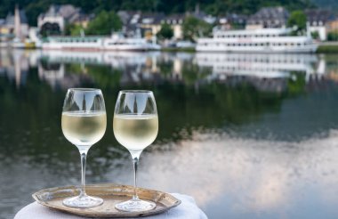 Mosel şarap bölgesinde beyaz kaliteli riesling şarabı tatmak için Mosel nehri ve Almanya 'nın güneşli günlerinde arka planda kalan eski Alman kasabası ile birlikte açık havada servis edilir.
