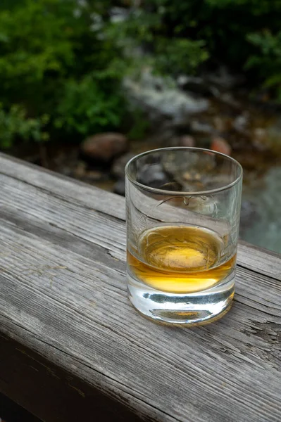 スコットランドを背景に流れるような渓流を背景にした強いスコッチシングルモルトウイスキーのグラス — ストック写真