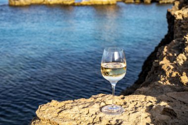 Kıbrıs 'taki Protaras turistik kasabası yakınlarındaki mavi deniz suyu manzaralı kayalarda bir bardak soğuk beyaz şarap servis ediliyor