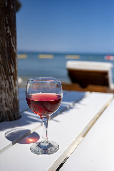 Drinking of cold rose wine in lounge bar on sunny sandy beach with blue sea water on background, summer vacation