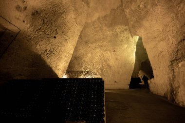 Derin ve uzun yeraltı mağaralarındaki raflarda şişeler şarap ve üzüm şarabından şampanya yapıyor Reims, Champagne, France 'ta.