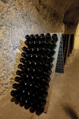 Derin ve uzun yeraltı mağaralarındaki raflarda şişeler şarap ve üzüm şarabından şampanya yapıyor Reims, Champagne, France 'ta.