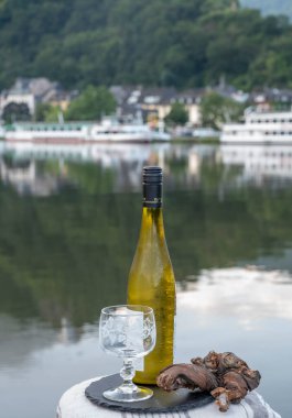 Mosel şarap bölgesinde beyaz kaliteli riesling şarabı tatmak için Mosel nehri ve Almanya 'nın güneşli günlerinde arka planda kalan eski Alman kasabası ile birlikte açık havada servis edilir.