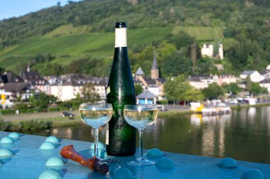 White quality riesling wine in green bottle served on old bridge across Mosel river with view on old German town in sunny day clipart