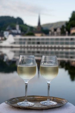 Mosel şarap bölgesinde beyaz kaliteli riesling şarabı tatmak için Mosel nehri ve Almanya 'nın güneşli günlerinde arka planda kalan eski Alman kasabası ile birlikte açık havada servis edilir.