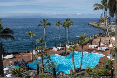 Atlantik Okyanusu kıyısında mavi yüzme havuzu ve palmiye ağaçları olan sahil kulübü, Costa Adeje, Tenerife, İspanya