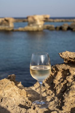 Kıbrıs 'taki Protaras turistik kasabası yakınlarındaki mavi deniz suyu manzaralı kayalarda bir bardak soğuk beyaz şarap servis ediliyor