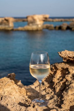 Kıbrıs 'taki Protaras turistik kasabası yakınlarındaki mavi deniz suyu manzaralı kayalarda bir bardak soğuk beyaz şarap servis ediliyor