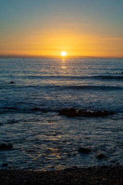Bir grup sörfçü kışın günbatımında Atlantik okyanusunun soğuk sularında tren kullanıyor, Playa de las Americas, Tenerife 'nin güneyi.