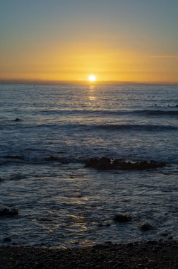 Bir grup sörfçü kışın günbatımında Atlantik okyanusunun soğuk sularında tren kullanıyor, Playa de las Americas, Tenerife 'nin güneyi.