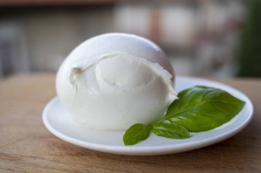 İtalyan yumuşak peynirli beyaz top Mozzarella di Bufala Campana ve taze yeşil fesleğen arka planda İtalyan evleriyle servis edilir.