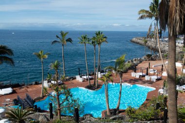 Atlantik Okyanusu kıyısında mavi yüzme havuzu ve palmiye ağaçları olan sahil kulübü, Costa Adeje, Tenerife, İspanya