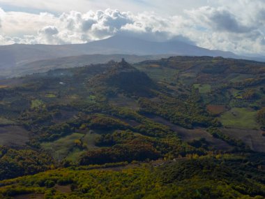 Bagno Vignoni, Tuscany, İtalya yakınlarındaki tepelerde hava panoramik manzarası. Selvi ağaçları, üzüm bağları, ormanlar ve bulutlu sonbaharda sürülen tarlalarla Toskana manzarası.