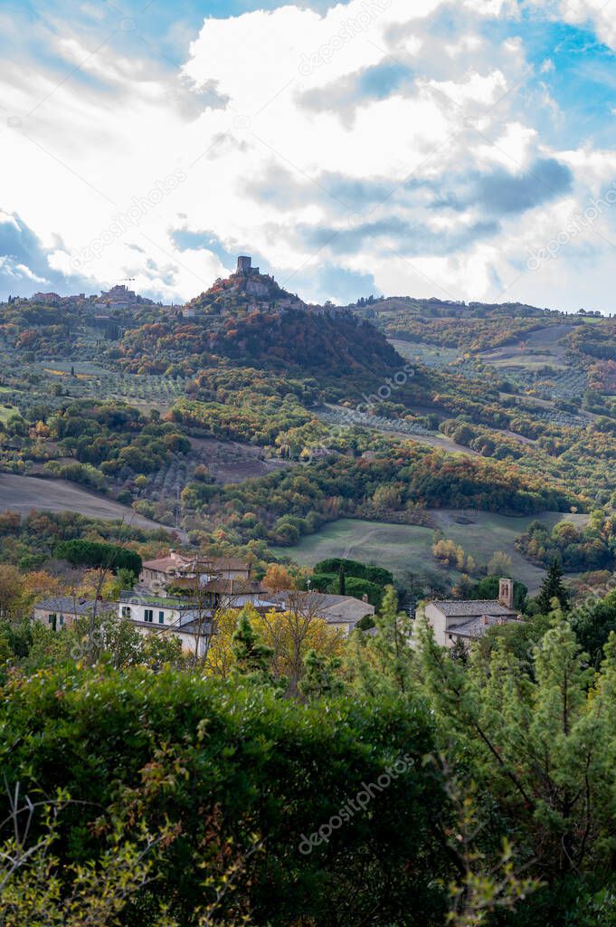Hiking on hills near Bagno Vignoni and view on Rocco Tuscany, Italy. Tuscan landscape with cypress trees, vineyards, forests and ploughed fields in cloudy autumn.