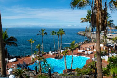Atlantik Okyanusu kıyısında mavi yüzme havuzu ve palmiye ağaçları olan sahil kulübü, Costa Adeje, Tenerife, İspanya