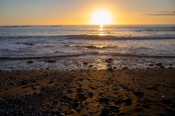 Group of surfers trains in cold water of Atlantic ocean on sunset in winter, Playa de las Americas, South of Tenerife