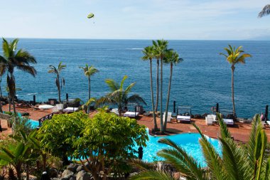 Atlantik Okyanusu kıyısında mavi yüzme havuzu ve palmiye ağaçları olan sahil kulübü, Costa Adeje, Tenerife, İspanya