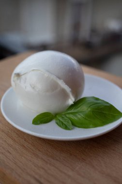 İtalyan yumuşak peynirli beyaz top Mozzarella di Bufala Campana ve taze yeşil fesleğen arka planda İtalyan evleriyle servis edilir.
