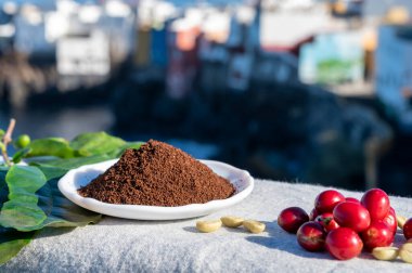 Olgun Arabika kahve meyveleri, yeşil kahve fasulyeleri, yapraklar ve kavrulmuş kahve kaseye yakın ve mavi okyanus manzaralı.