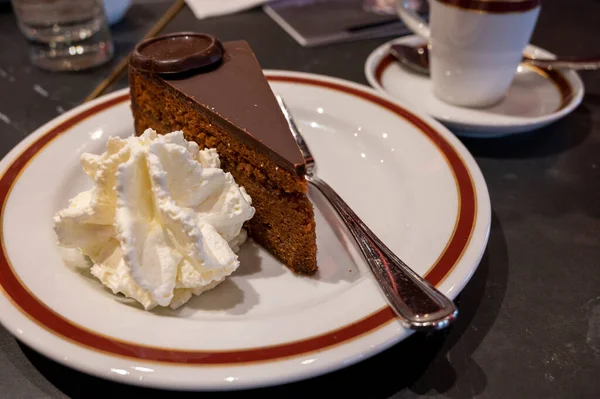 Meşhur Sachertorte çikolatalı pastası. Kayısı reçeli ve beyaz tahtada krem şanti ile servis ediliyor.