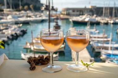 Soğuk gül Provencal şarabı bardaklarla sunuluyor. Açık terasta sunuluyor. Eski balıkçıların limanında, Cassis, Provence, Fransa 'da renkli tekneleri var.