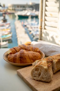 Provence 'de yaz sabahı, taze kruvasan ve baget ekmeği ile geleneksel kahvaltı Cassis, Provence, Fransa Limanı' ndaki balıkçı teknelerinin manzarası.