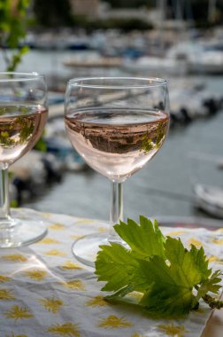 Açık terasta sunulan Rose Provencal şarabı Cassis, Provence, Fransa 'da renkli tekneleri olan eski balıkçıların limanına bakıyor.