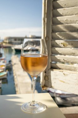 Soğuk gül şarabı, cam içinde sunulan güneş ışığı eşliğinde açık terasta, Cassis, Provence, Fransa 'da eski balıkçıların limanında renkli teknelerle sunuluyor.
