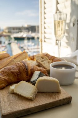 Fransız kahvaltısında taze kruvasan, baquett ekmeği, crottin keçi peyniri, sade kahve ve Cassis, Provence, Fransa 'daki balıkçı tekneleri manzaralı. Provence 'de Tatil.