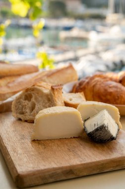 Provence 'de güneşli bir sabah, taze kruvasan, baquett ekmeği, crottin keçi peyniri ve Cassis, Provence, Fransa limanındaki balıkçı tekneleri manzaralı bir kahvaltı.