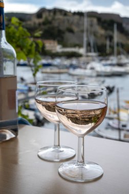 Açık terasta sunulan Rose Provencal şarabı Cassis, Provence, Fransa 'da renkli tekneleri olan eski balıkçıların limanına bakıyor.