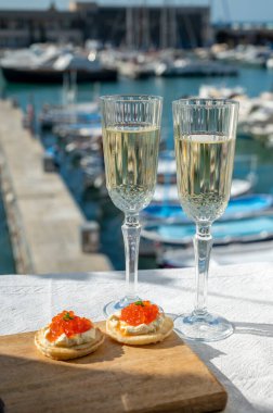 Ekşi krema ve tuzlu somon kırmızısı havyar ve Fransız şampanyası brut köpüklü şarap ile küçük krep çiftleri Cassis, Provence, Fransa 'nın limanındaki renkli teknelerde servis edilir.